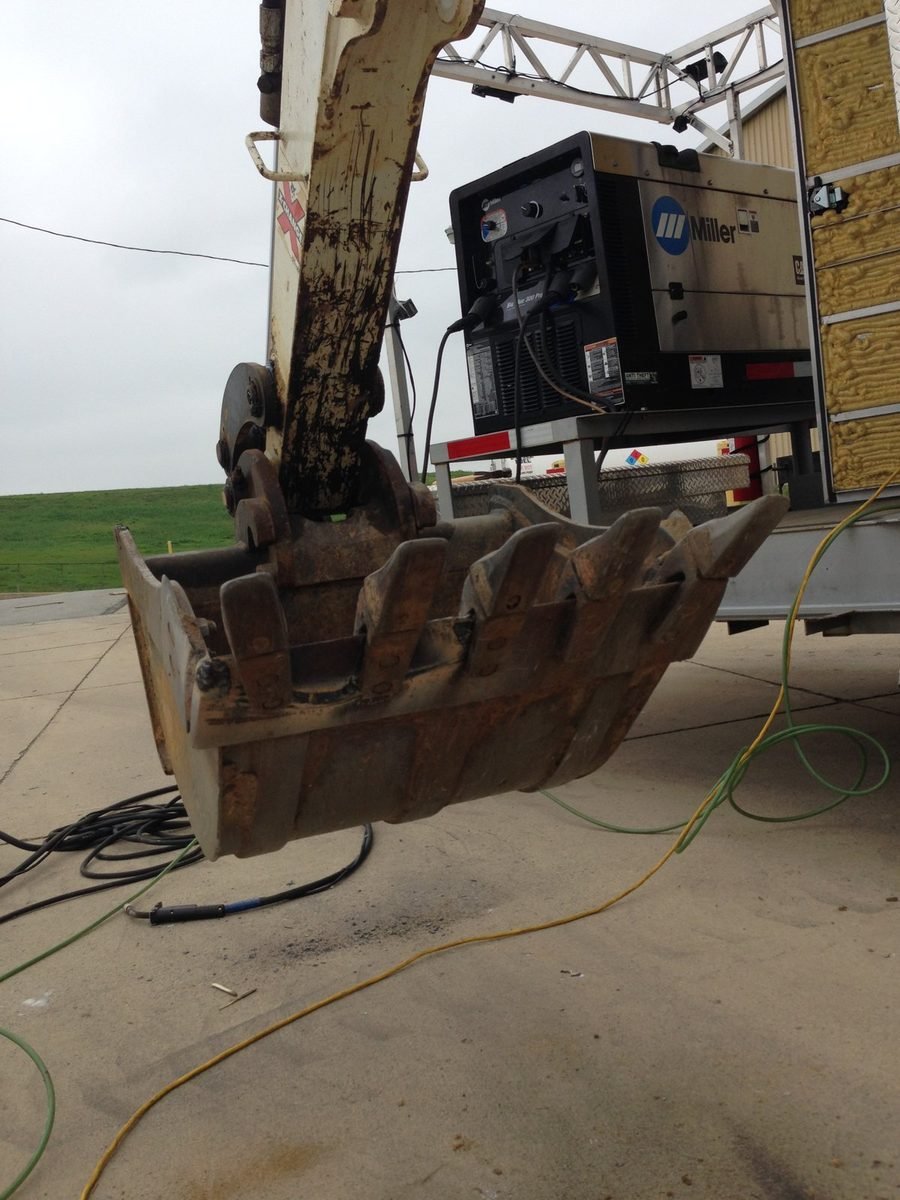 Excavator bucket with teeth in for on-site welding repair next to a mobile welder